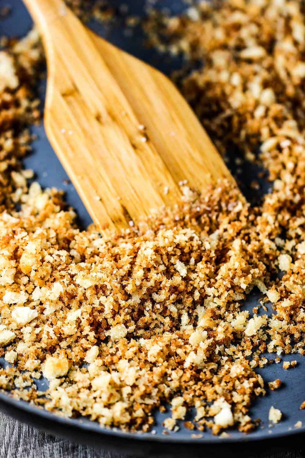 A skillet of toasted bread crumbs with a wooden spoon. 