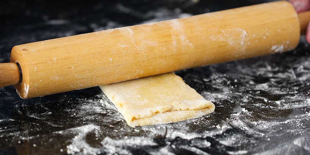 A rolling pin flattening a folded piece of pasta dough. 