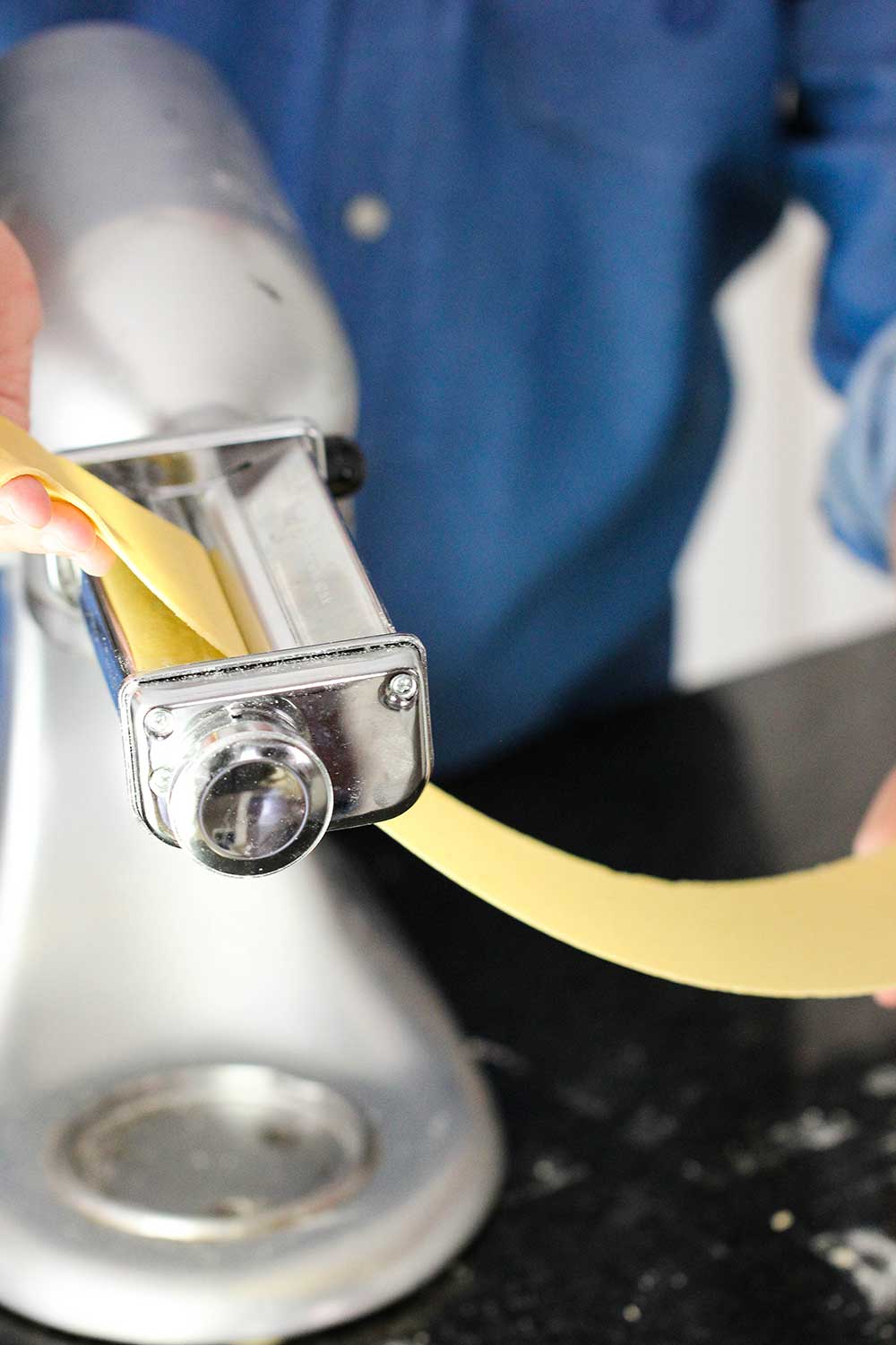 A sheet of homemade pasta being put through a pasta roller on a stand mixer. 