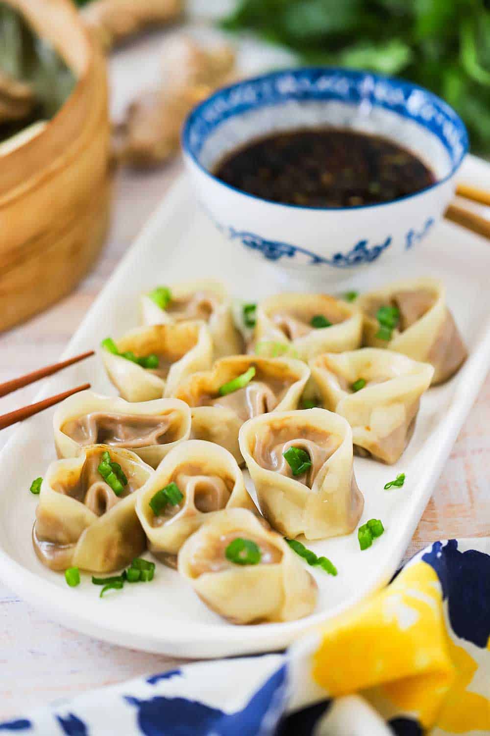 Vegetarian Steamed Dumplings sitting in a bamboo steamer basket next to an Asian-style bowl filled with soy dipping sauce next to chop sticks. 