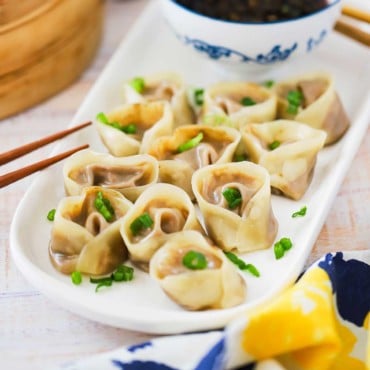 An oval white serving platter filled with vegetarian steamed dumplings sprinkled with chopped parsley.