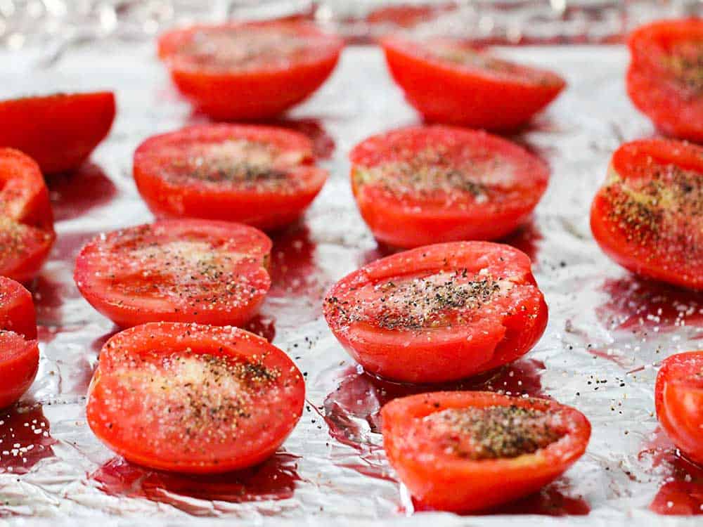 A baking sheet lined with foil filled with cut tomatoes to be roasted. 