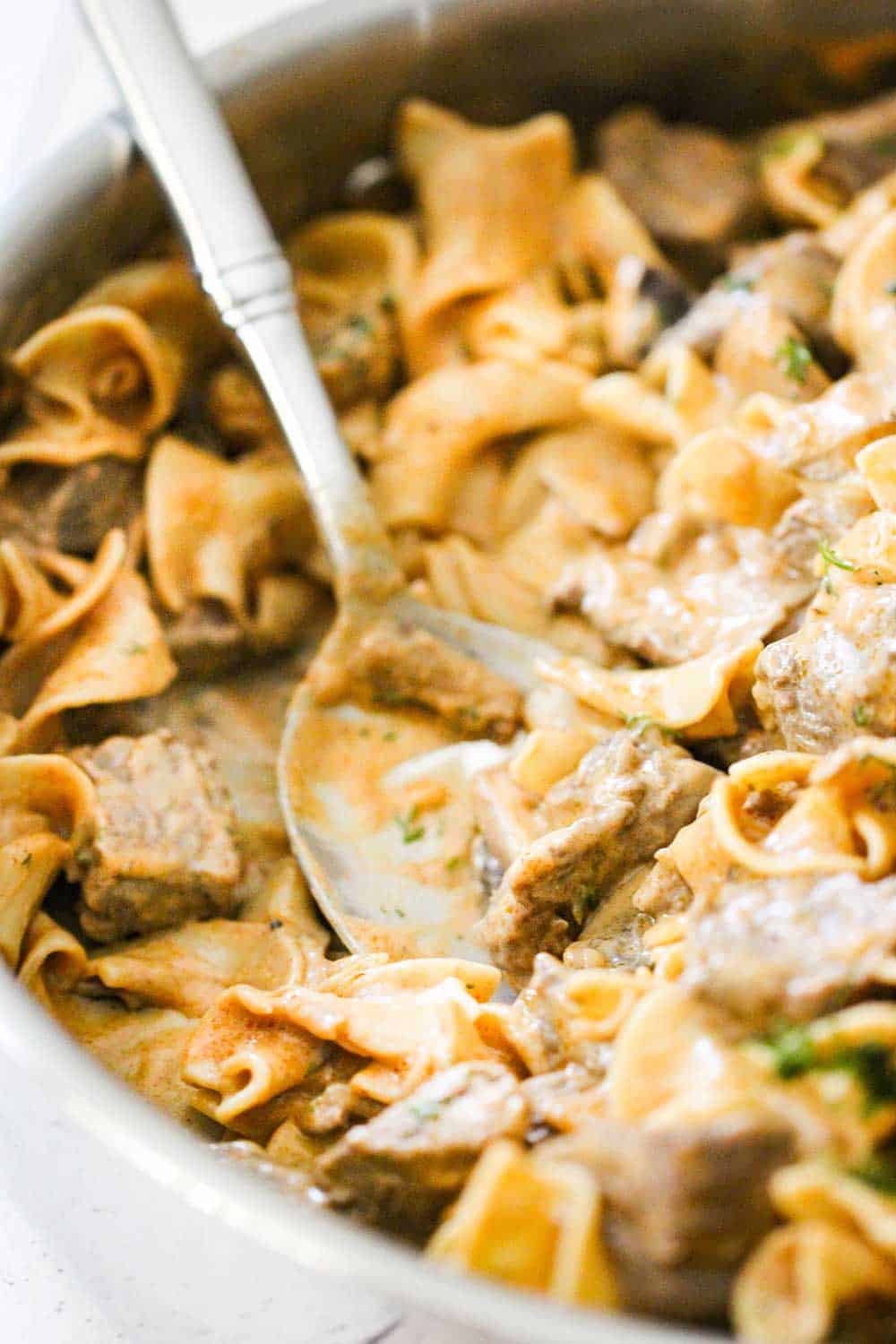 A spoon in a large skillet of gourmet beef stroganoff.