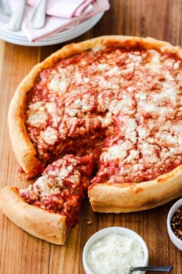 A Chicago-Style Deep Dish Pizza on a cutting board with a slice pulled out next to Parmesan cheese.