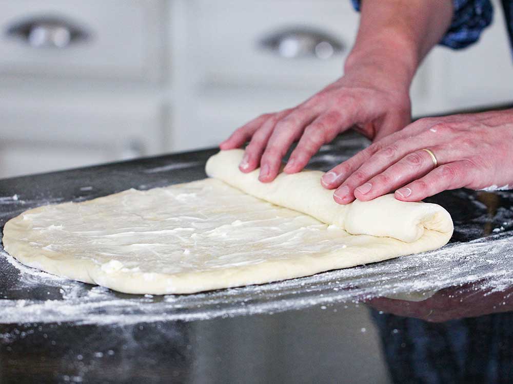 Two hands rolling pizza dough on a floured surface. 