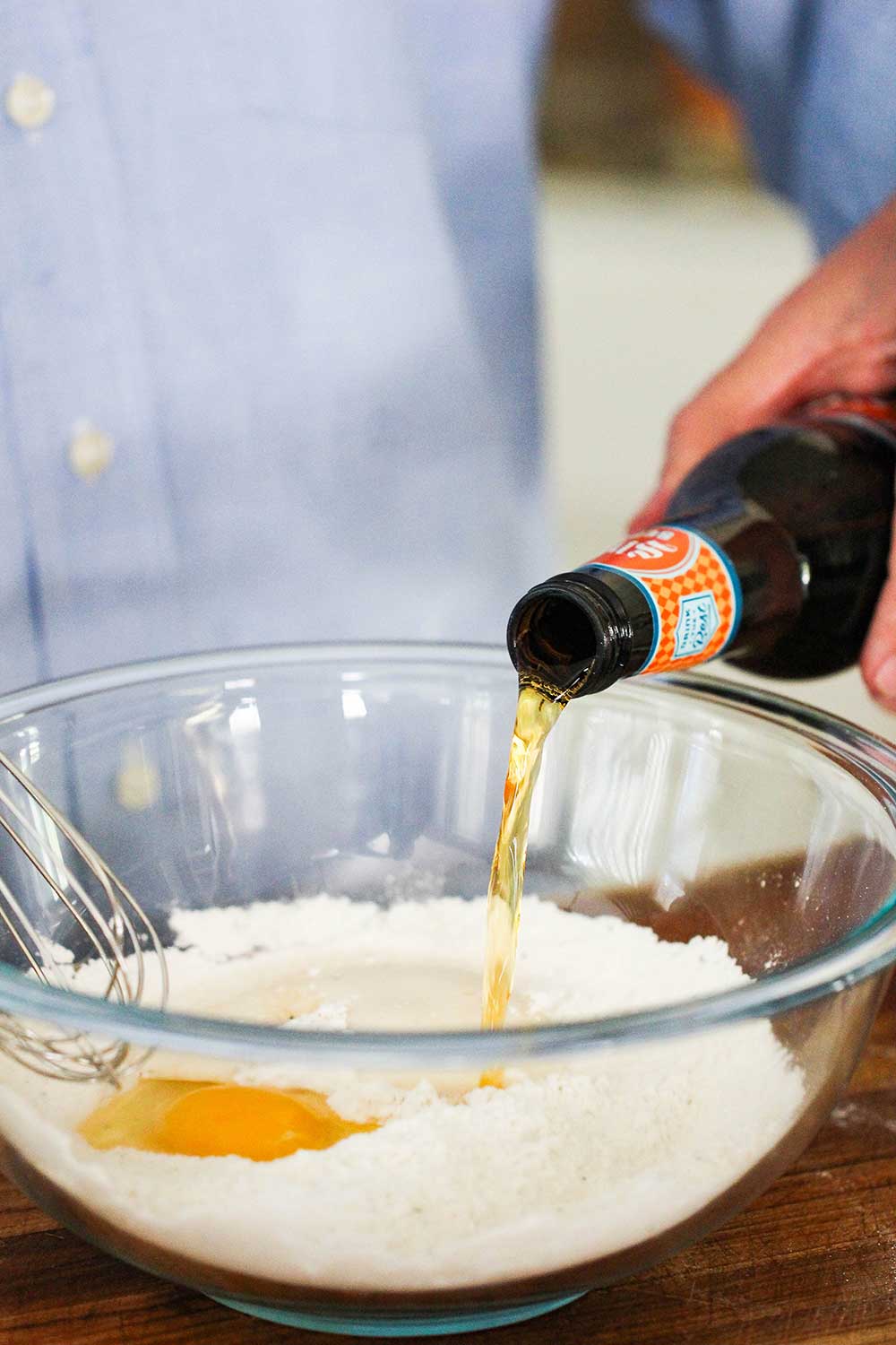 A bottle of beer being poured into a batter for fried fish. 
