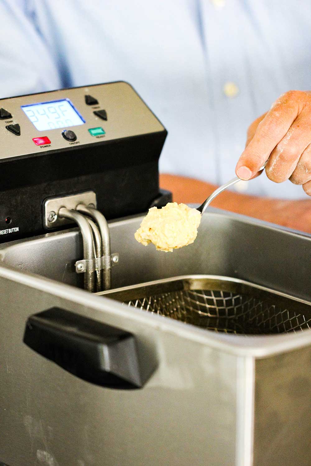 A spoon with hush puppies batter on it over a deep fryer. 