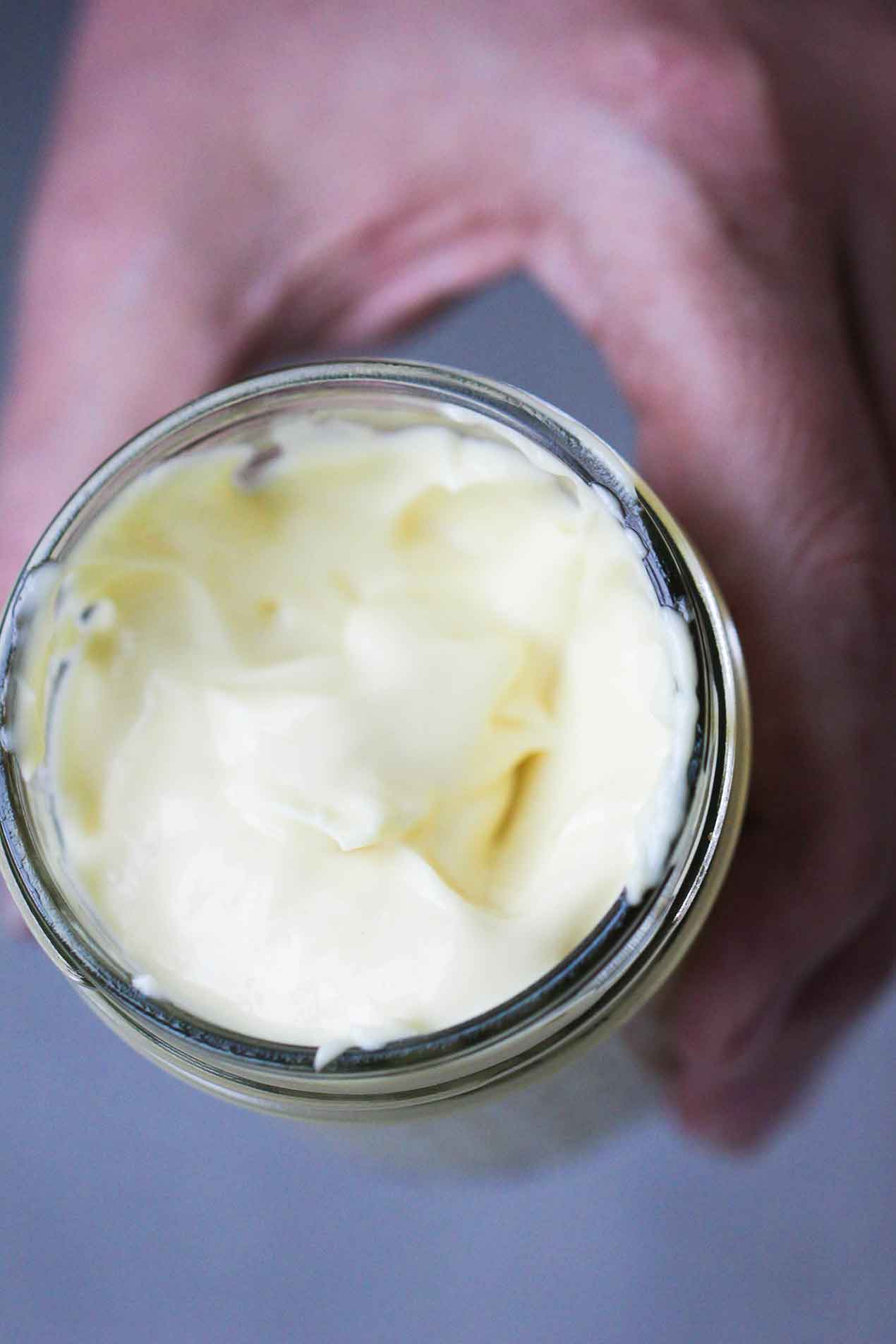 A hand holding a jar of homemade mayonnaise