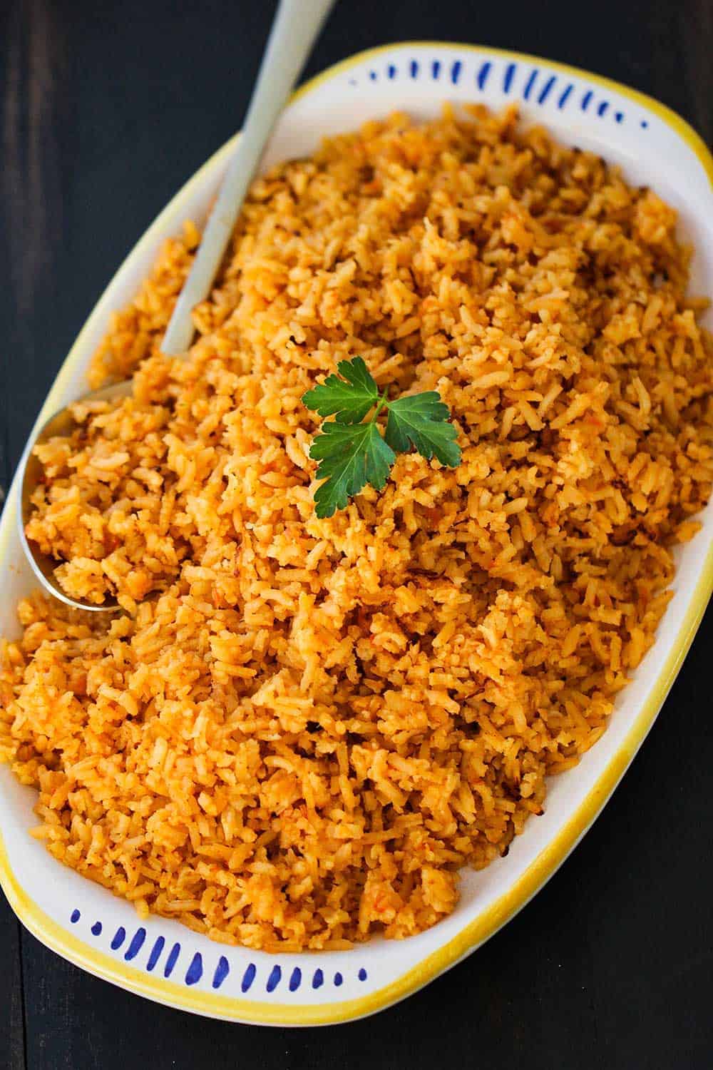 A white platter holding a Mexican rice with a spoon next to it. 