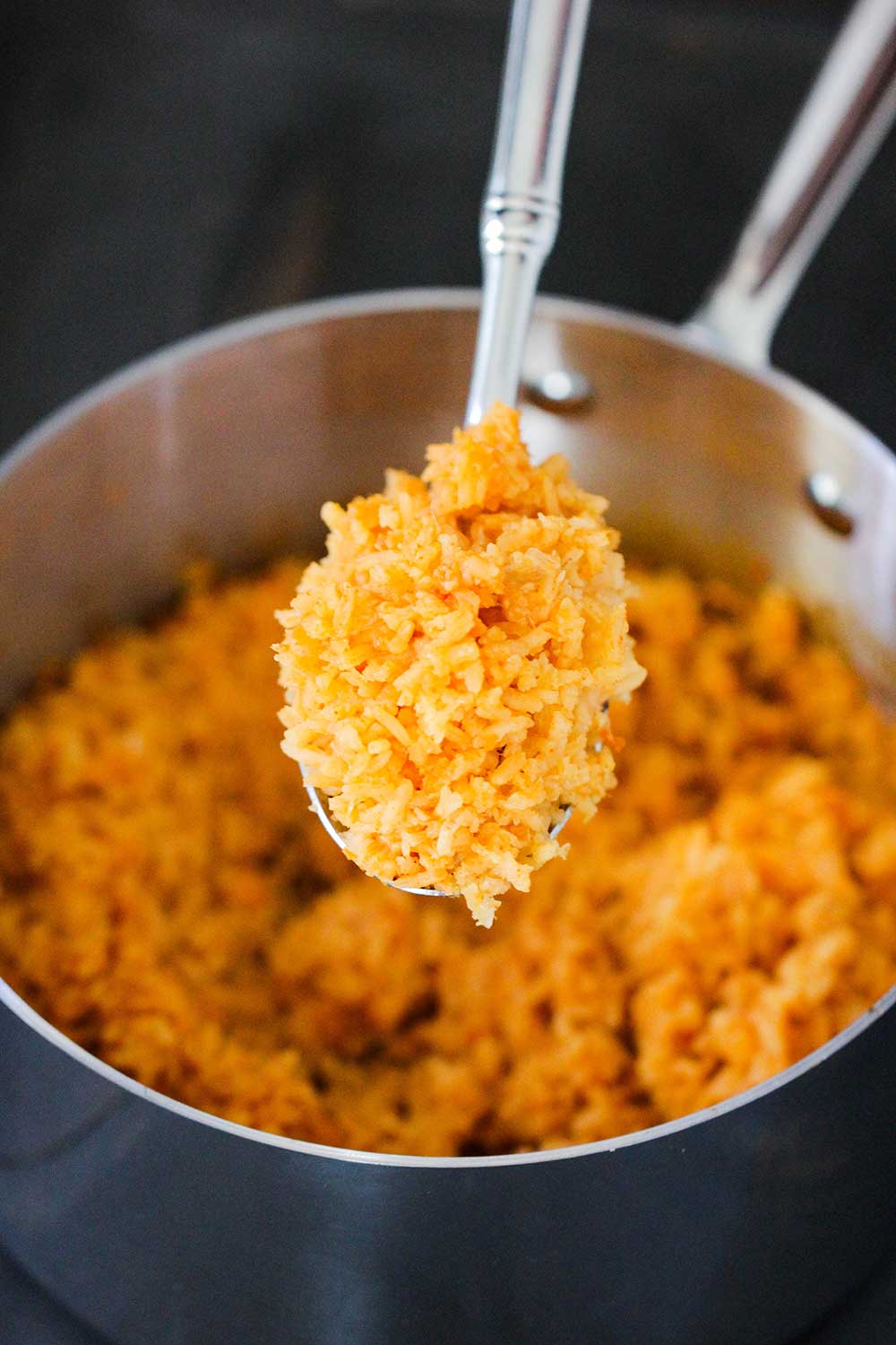A spoon holding a helping of Mexican rice over a pan. 