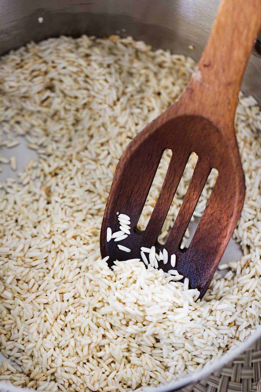 A wooden spoon in saucepan filled with long-grain white rice. 