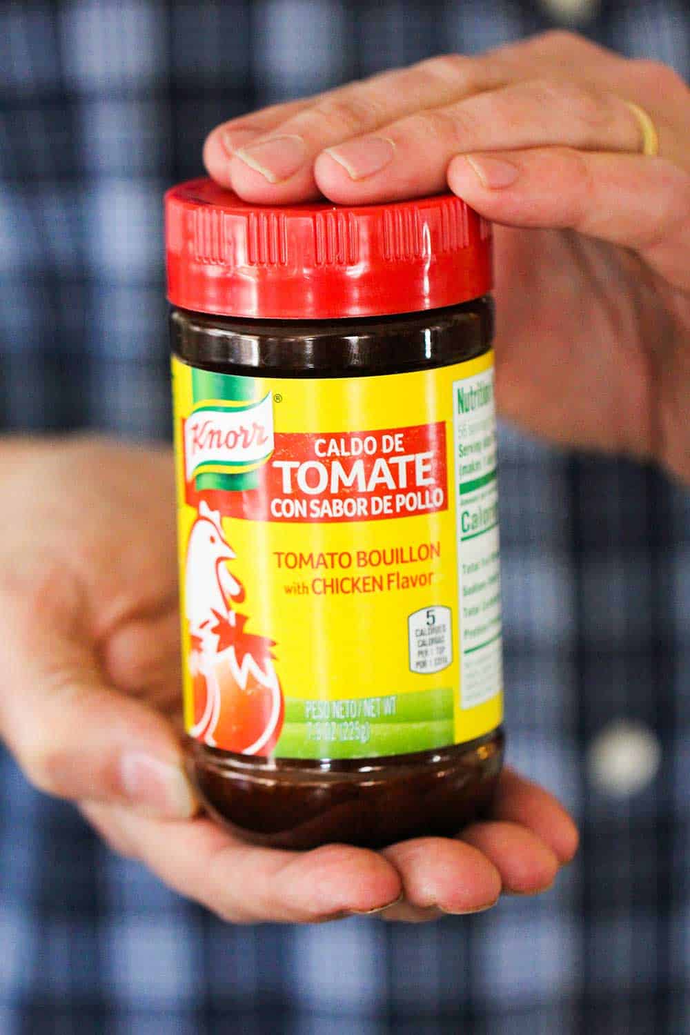 Two hands holding a bottle of Caldo de Tomate. 