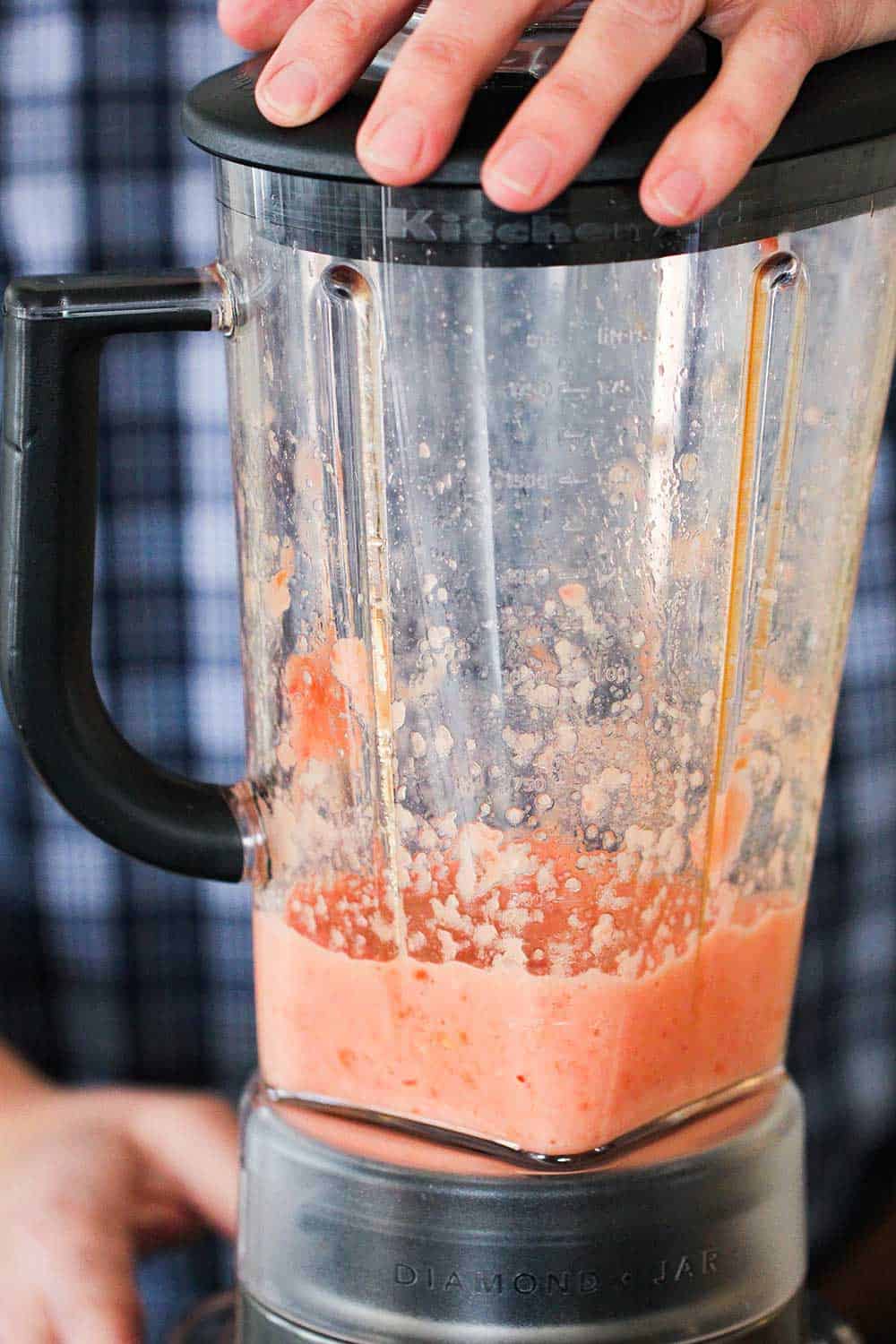 Two hands holding a blender that has puréed tomatoes and onions in it. 