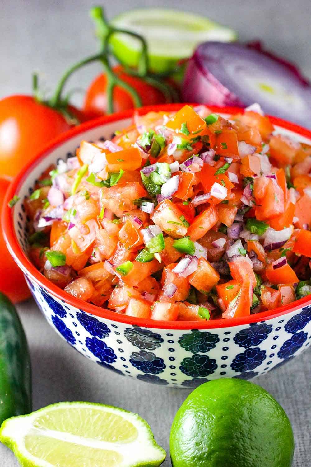 Fresh Pico de Gallo in a colorful bowl next to sliced limes. 