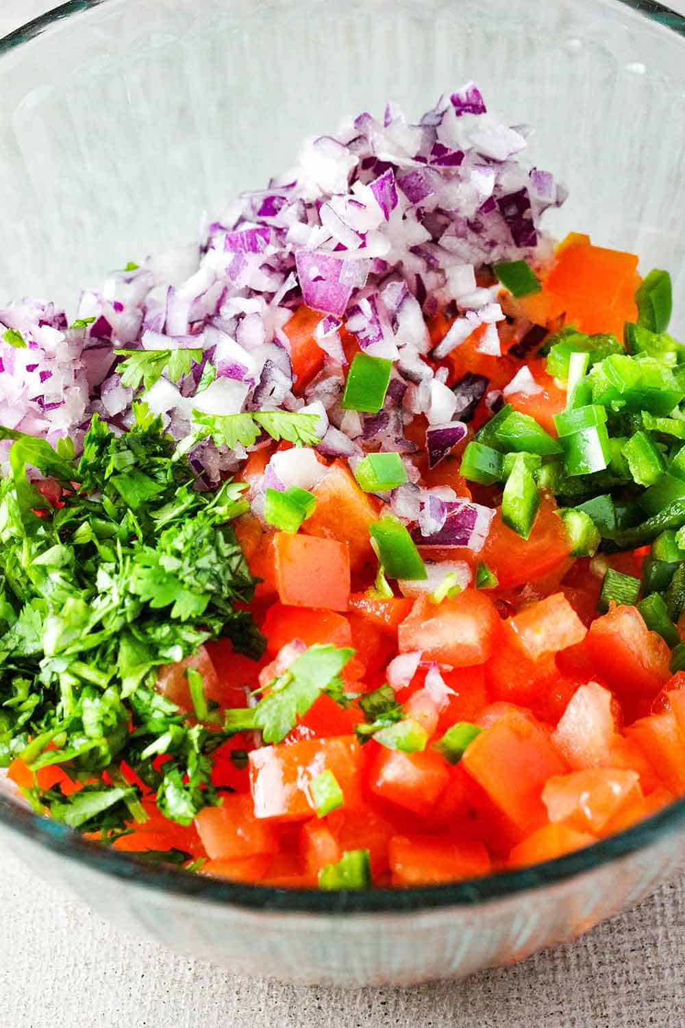 Chopped tomatoes, cilantro, red onion and jalapeño in a glass bowl for pico de Gallo.