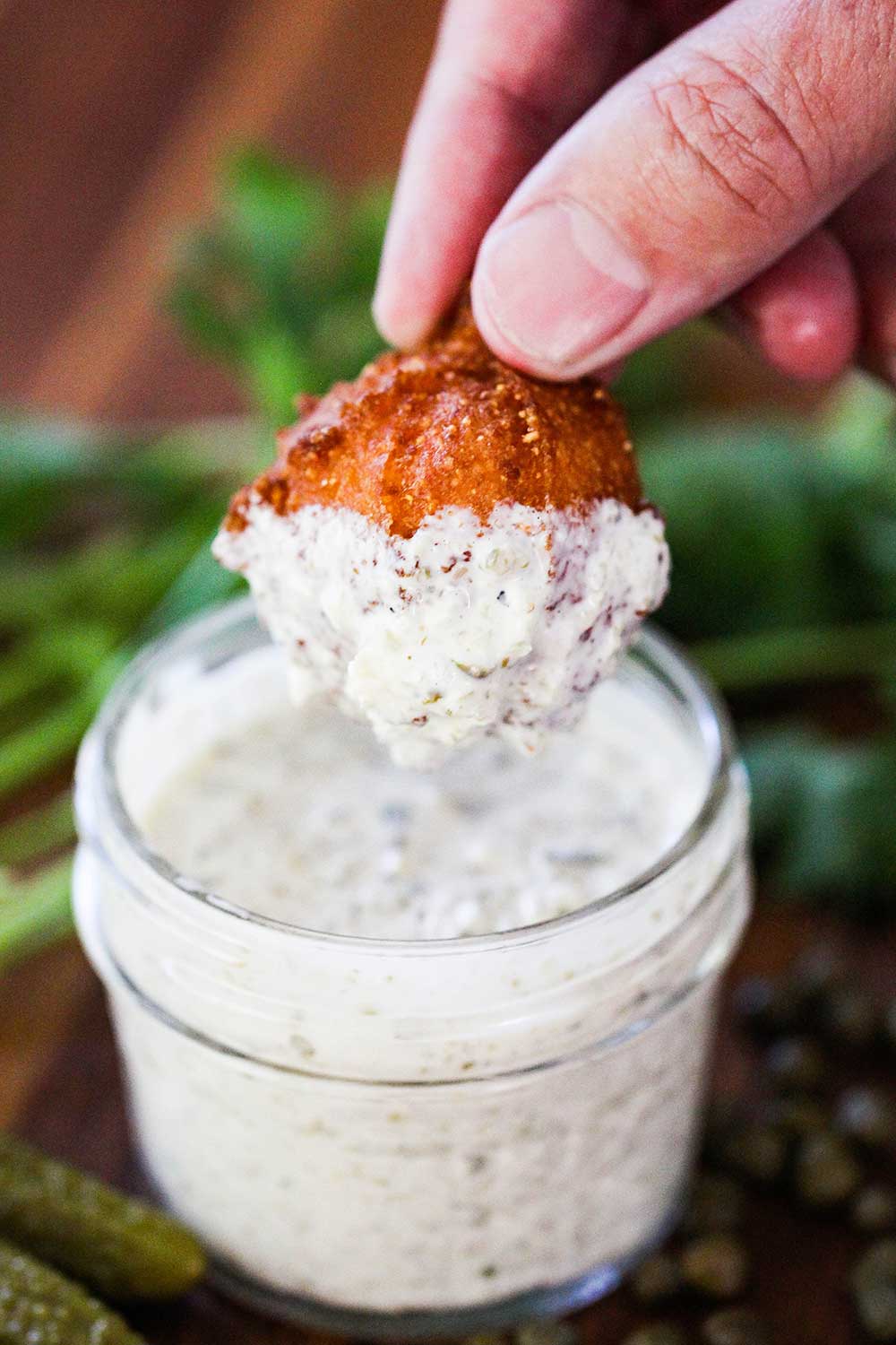 A hand holding a fried hush puppy that has been dipped into tartar sauce. 