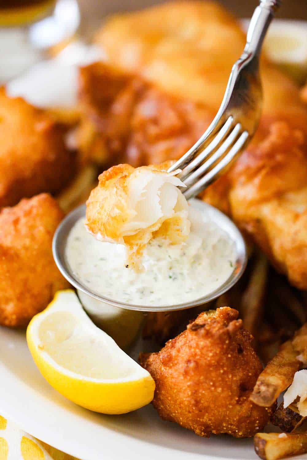 A piece of fried fish in a fork dipped into homemade tartar sauce. 