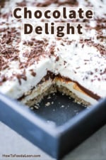 A square metal baking pan filled with a dessert that is layered with shortbread crust, cream cheese, chocolate pudding, and whipped cream.