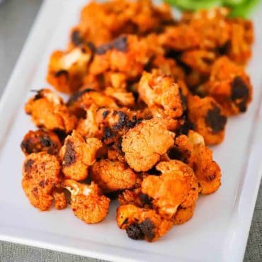 A white platter filled with buffalo cauliflower bites.