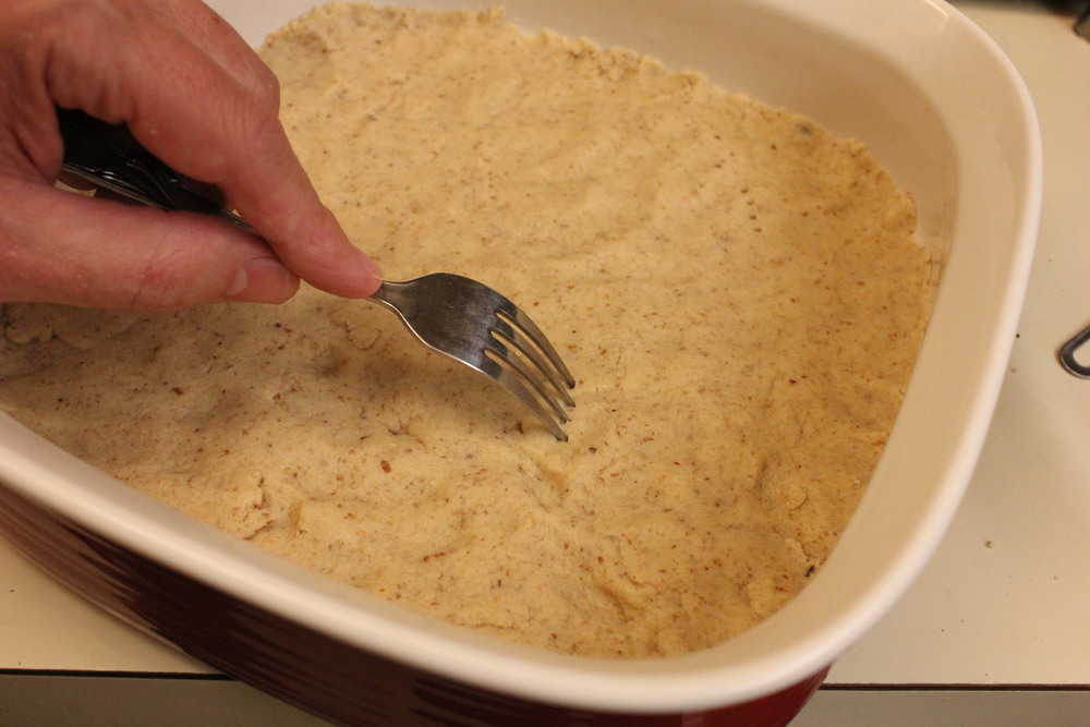 A hand using a fork to poke holes in shortbread crust.