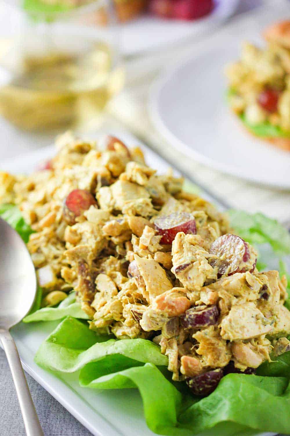 A mound of curry chicken salad on a bed of lettuce on a white platter. 