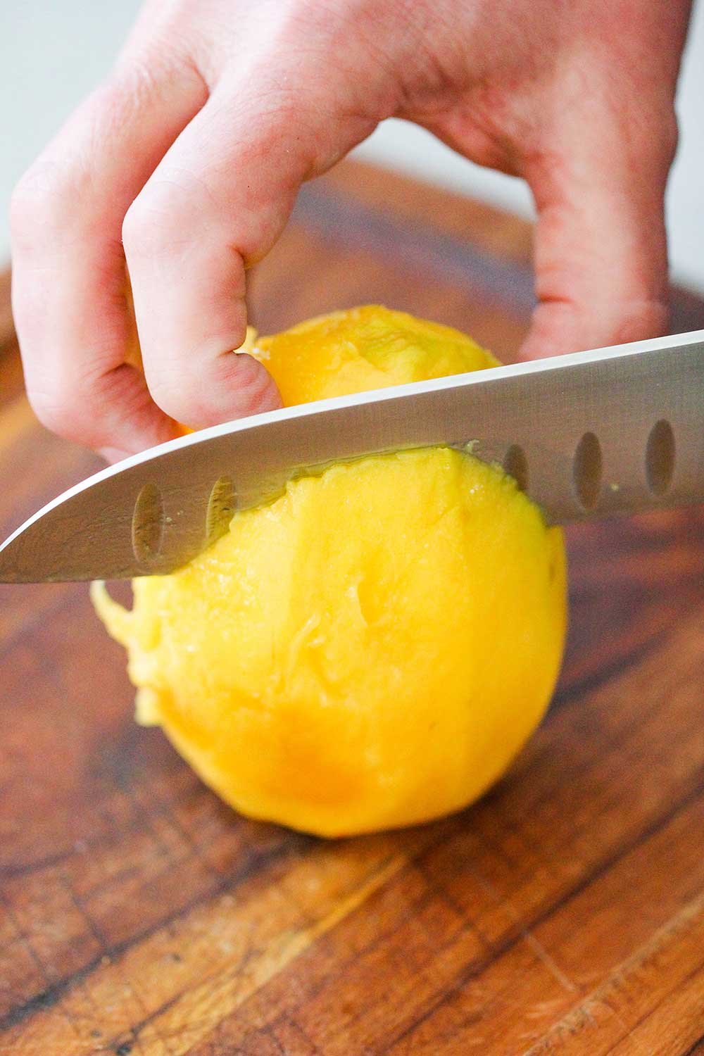 A hand using a large chef's knife to slice a fresh mango on a cutting board. 