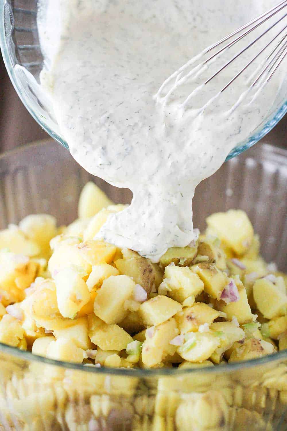 Dill and dijon dressing being pour onto cooked potatoes for potato salad.