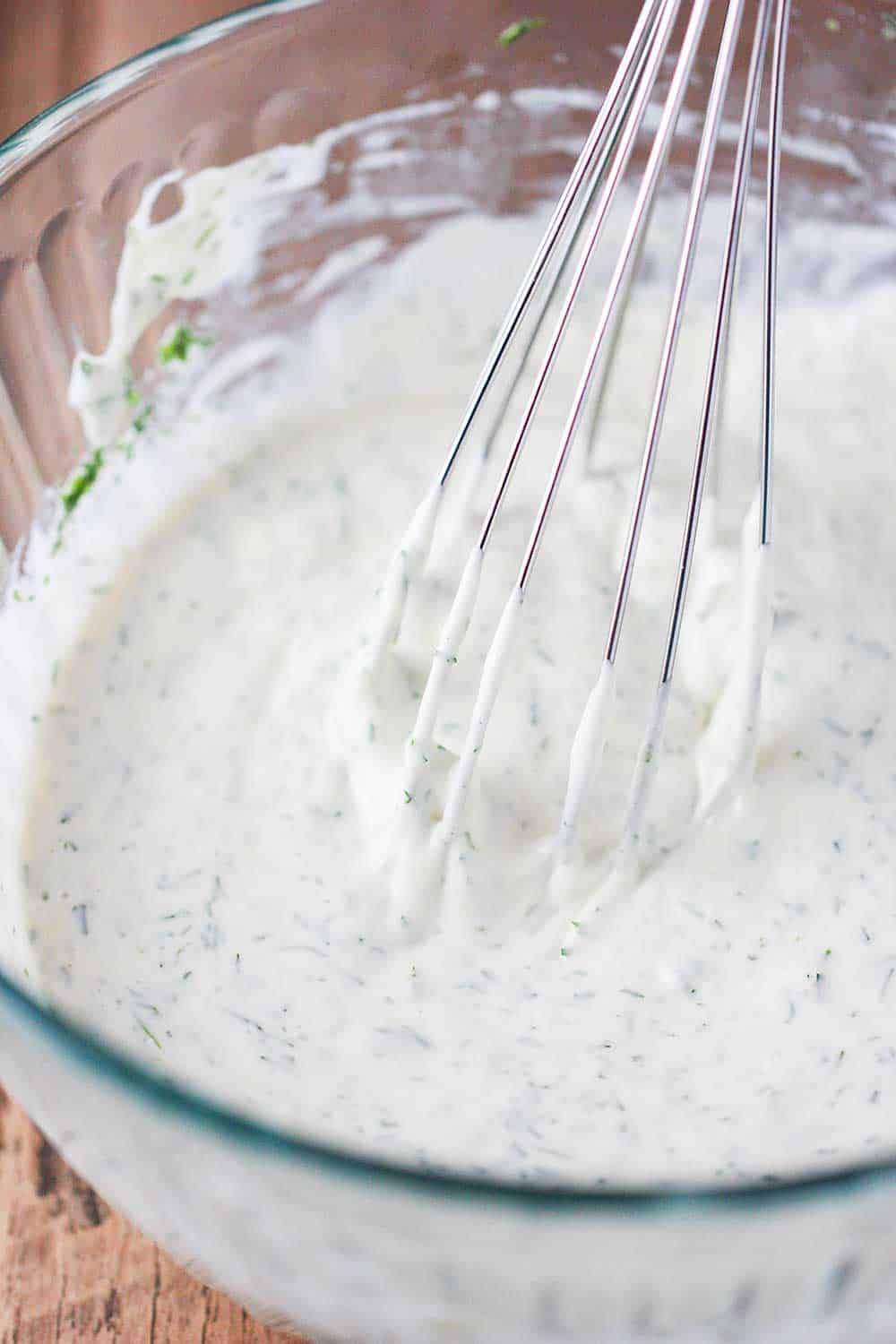 A glass bowl of dressing with a whisk for potato salad. 