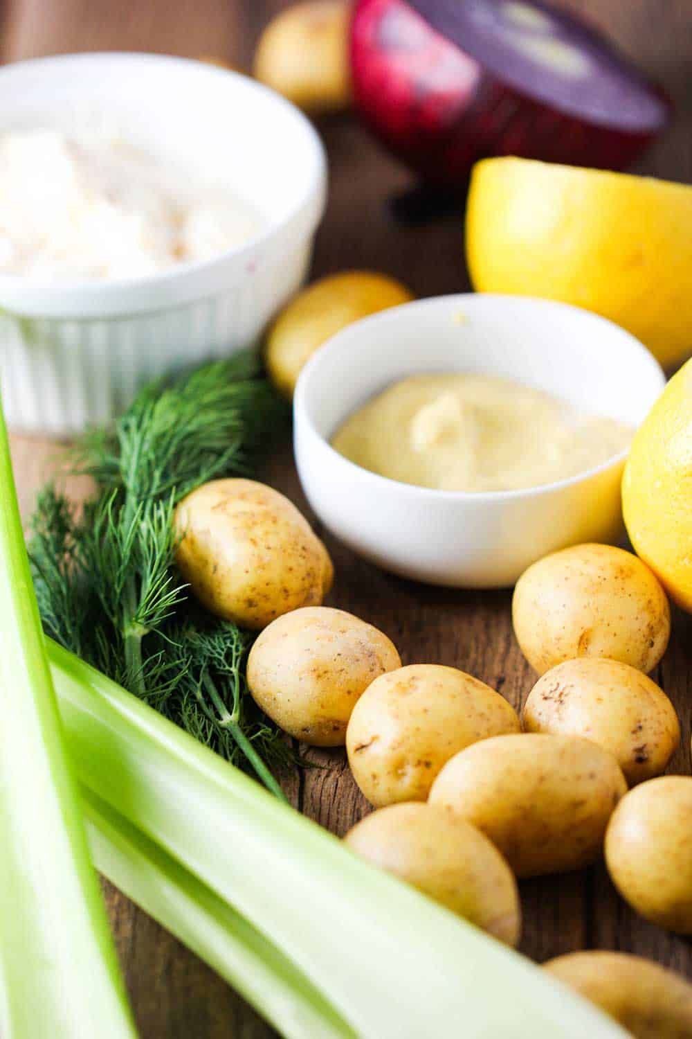 Fresh potatoes, celery, Dijon and lemon on a cutting board for best-ever potato salad. 