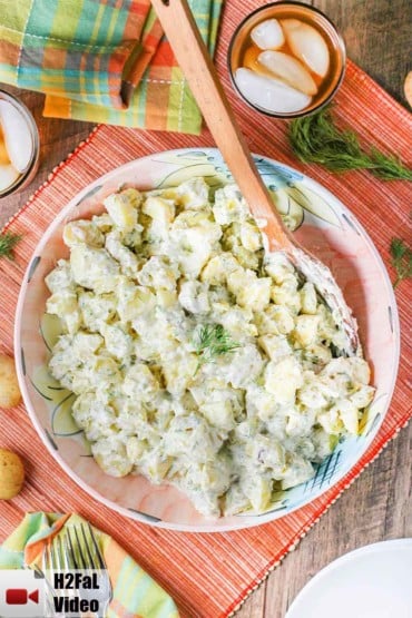 Creamy potato salad in a large pink bowl with a wooden spoon.
