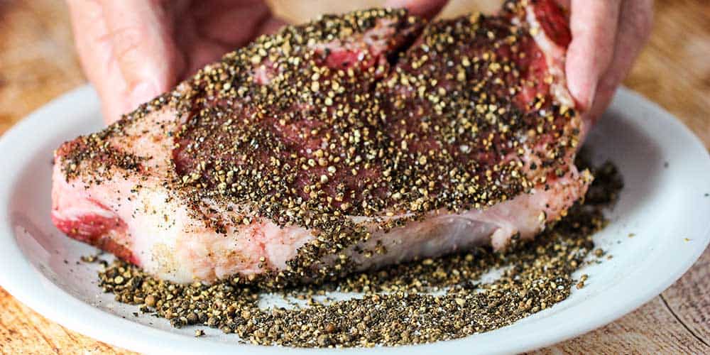 Cover the strip steak all over with the cracked black peppercorns. 