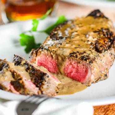 Sliced strip steak with au poivre sauce poured over the top.