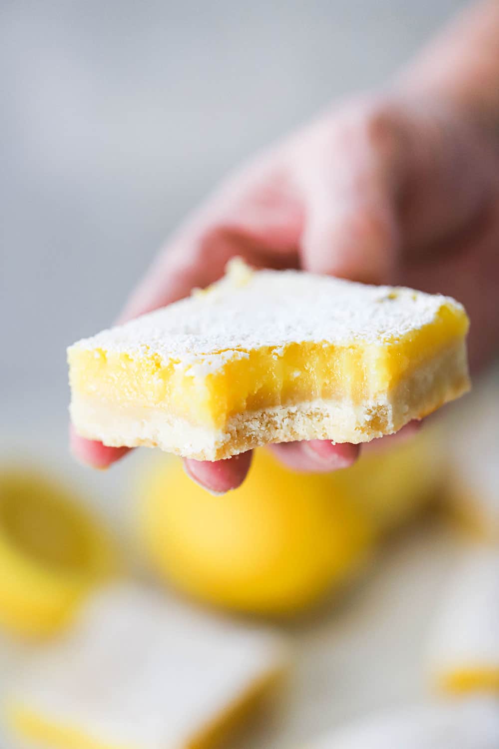 A person holding a lemon bar with a bit taken out of the corner of it. 