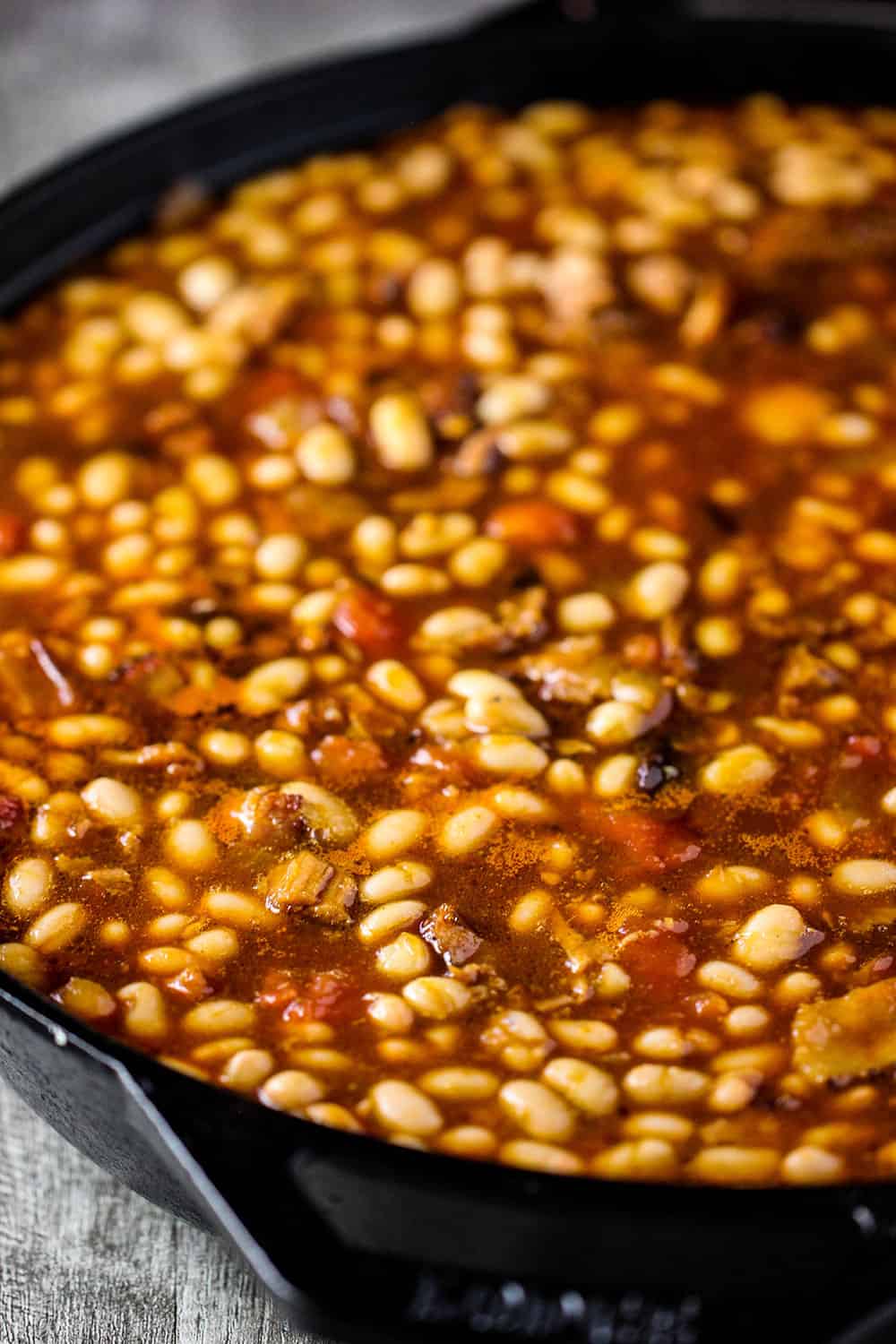 Pre-cooked beans in a sauce in a large cast iron skillet for Southern Baked Beans. 