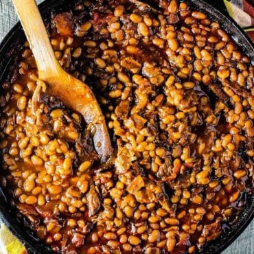 Southern baked beans in a cast iron skillet with a wooden spoon.