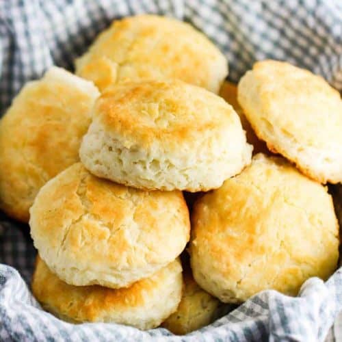 A pile of Homemade Southern biscuits in a basket lined with a checkered cloth.