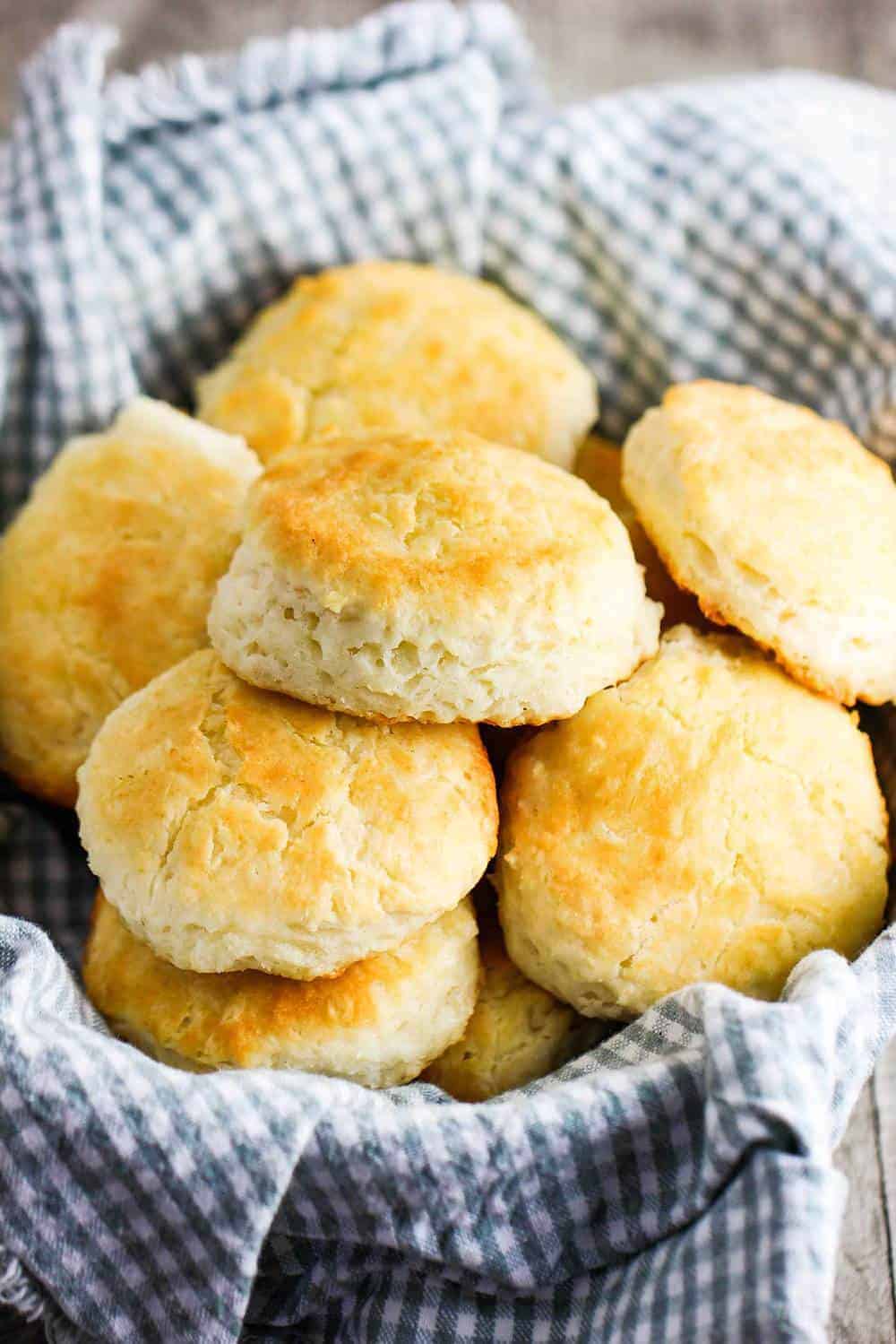 A pile of Homemade Southern biscuits in a basket lined with a checkered cloth. 