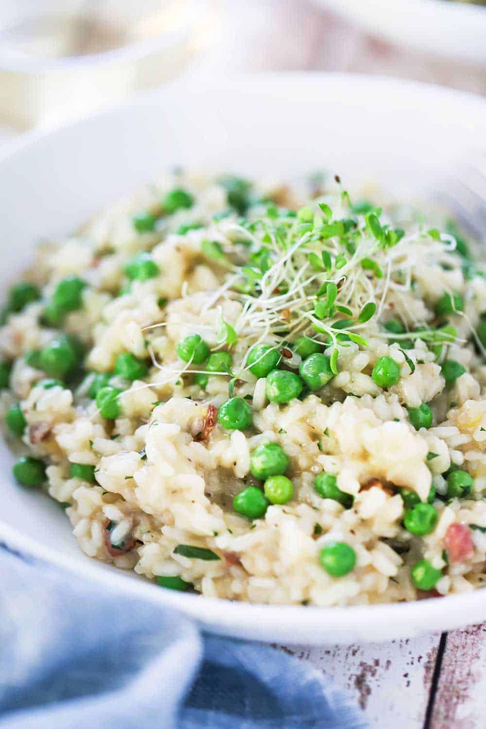 A white individual bowl filled with risi e bisi and topped with pea shoots. 