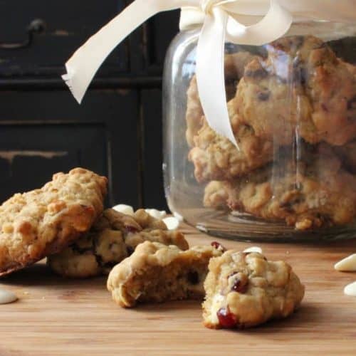 Oatmeal, Cranberry and White Chocolate Chunk Cookies on a wood cutting board next to a jar filled with cookies