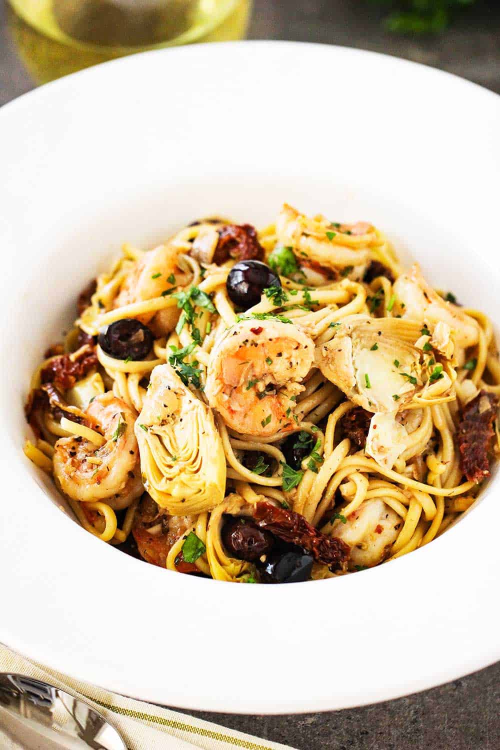A white bowl with a large edge holding Mediterranean pasta with shrimp.
