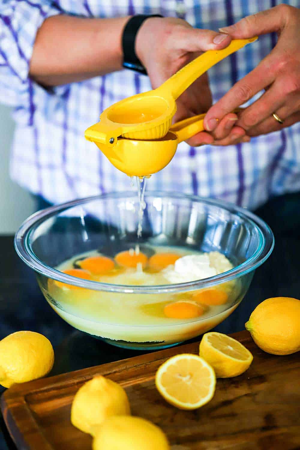 A person using a citrus press to squeeze fresh lemon juice into a bowl filled with eggs, sugar, and flour. 