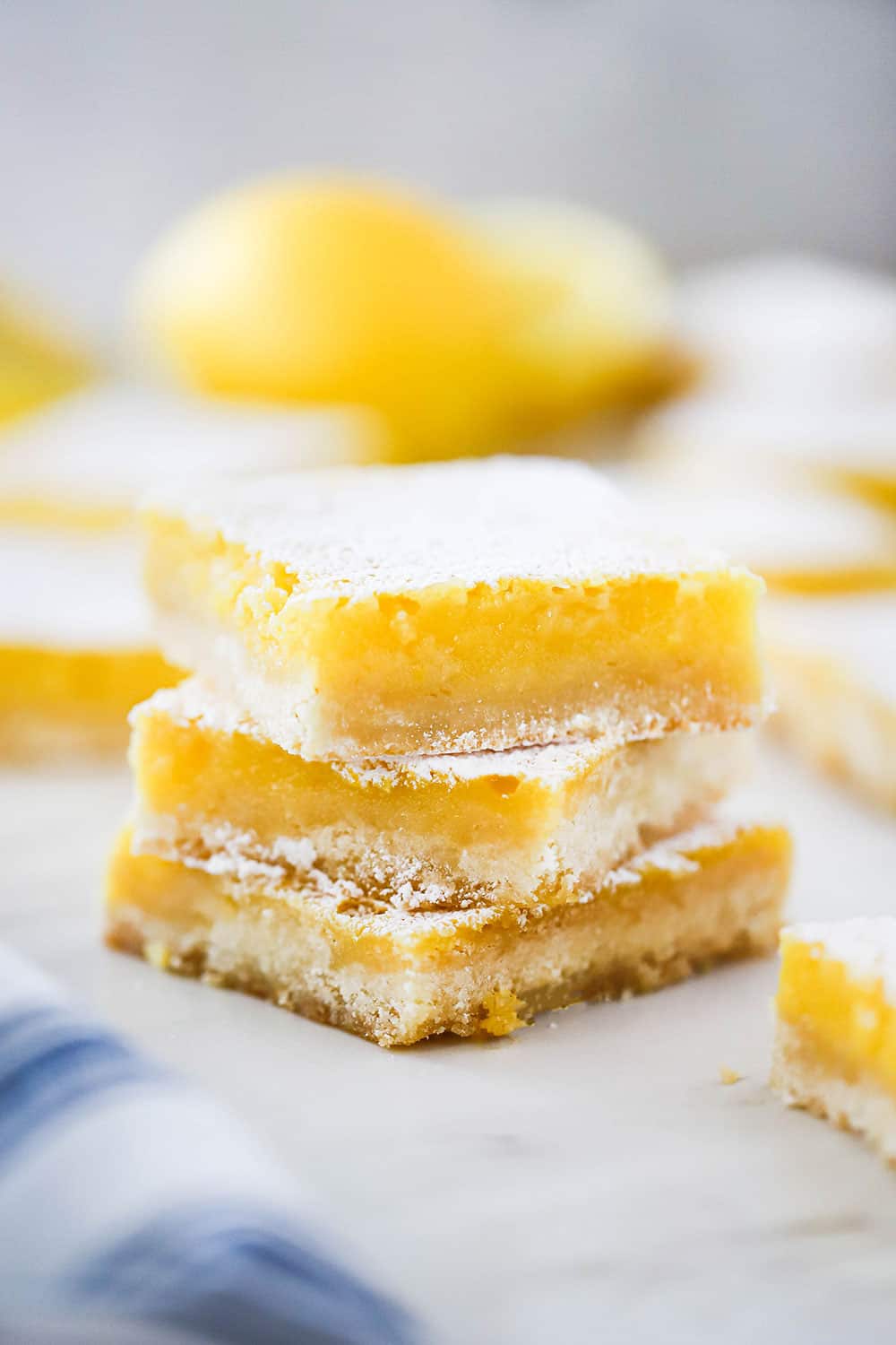 A stack of 3 lemon bars sitting on a piece of parchment paper. 