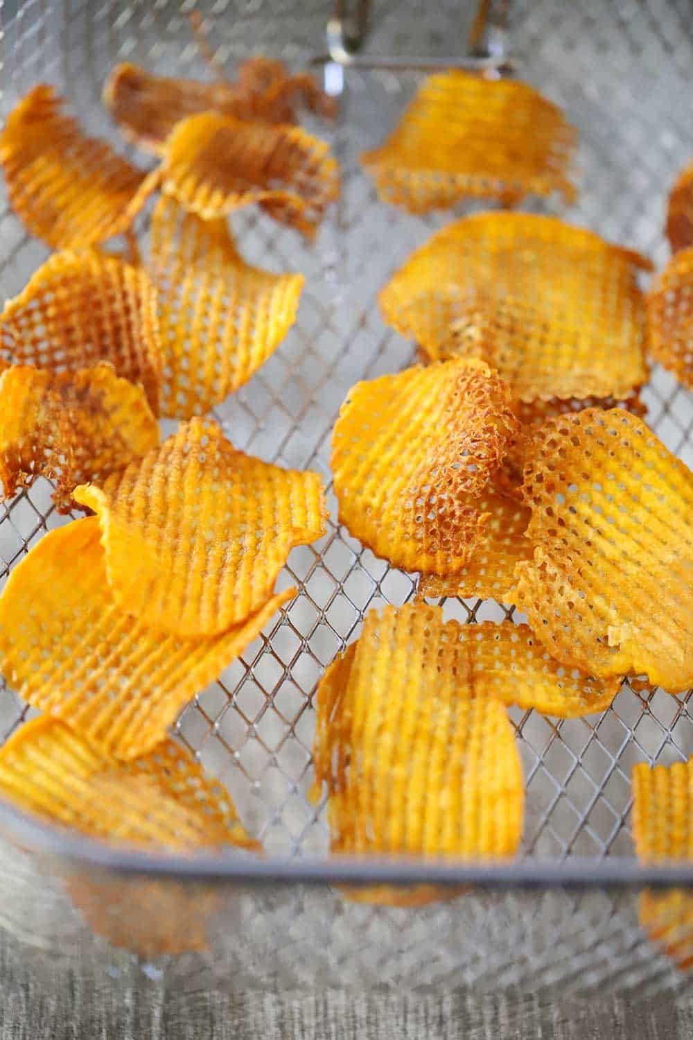 A metal fry basket holding freshly fried crosshatch sweet potato chips. 