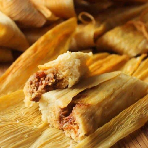Homemade tamales with pork filling on a board in wrappers