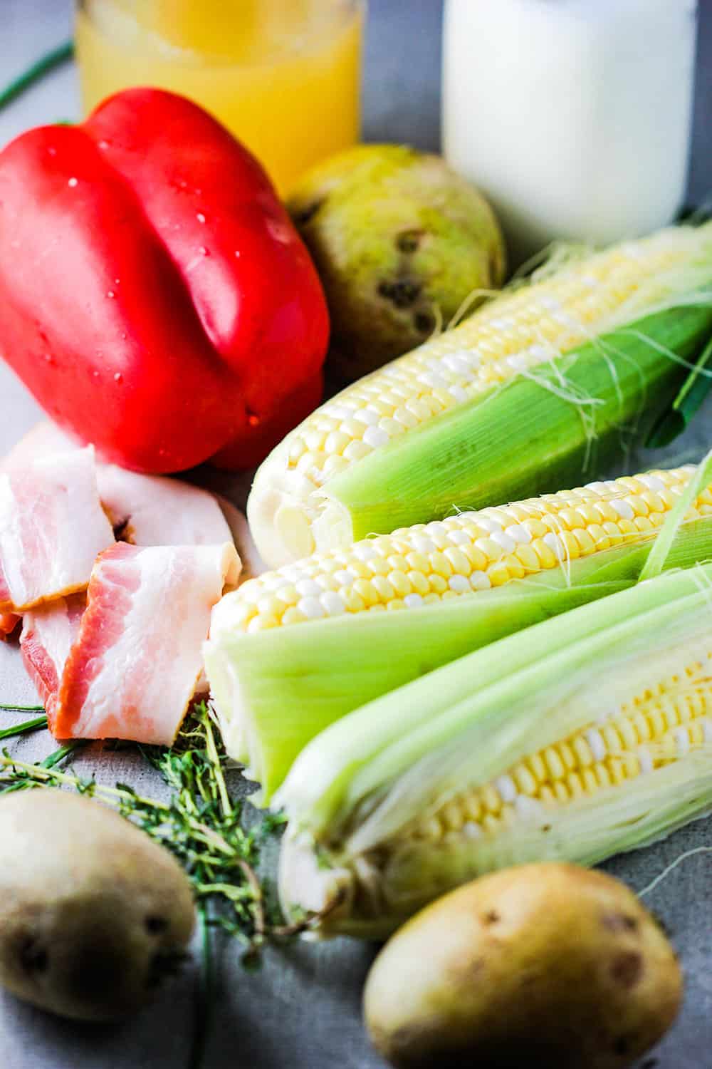 Ears of corn, potatoes, uncooked bacon and red bell pepper for corn chowder. 