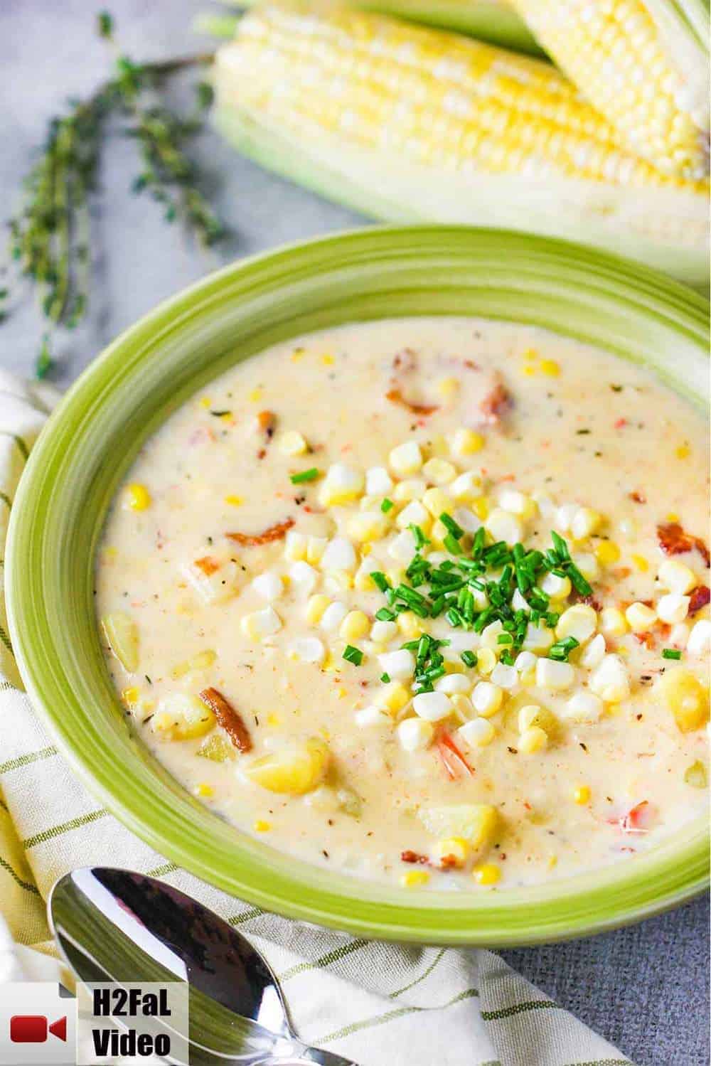 A green bowl full of farm fresh corn chowder with ears of corn nearby. 