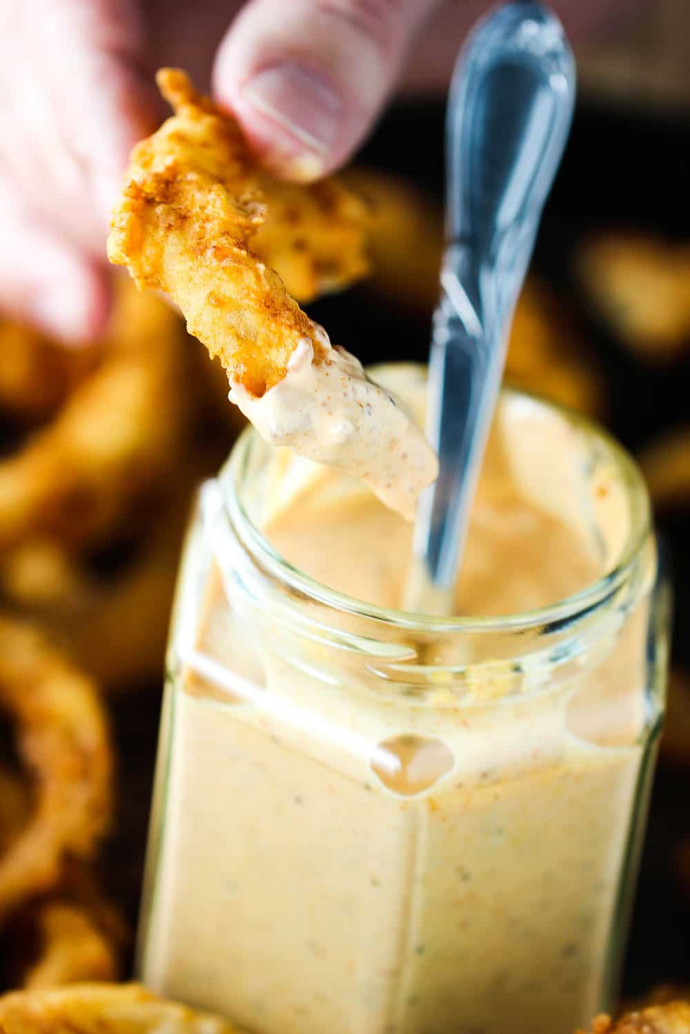 Onion ring dipping into a jar of remoulade sauce