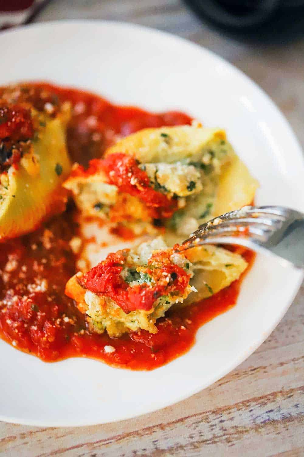 A fork being used to break open a stuffed shell on marinara sauce all on a white dinner plate. 