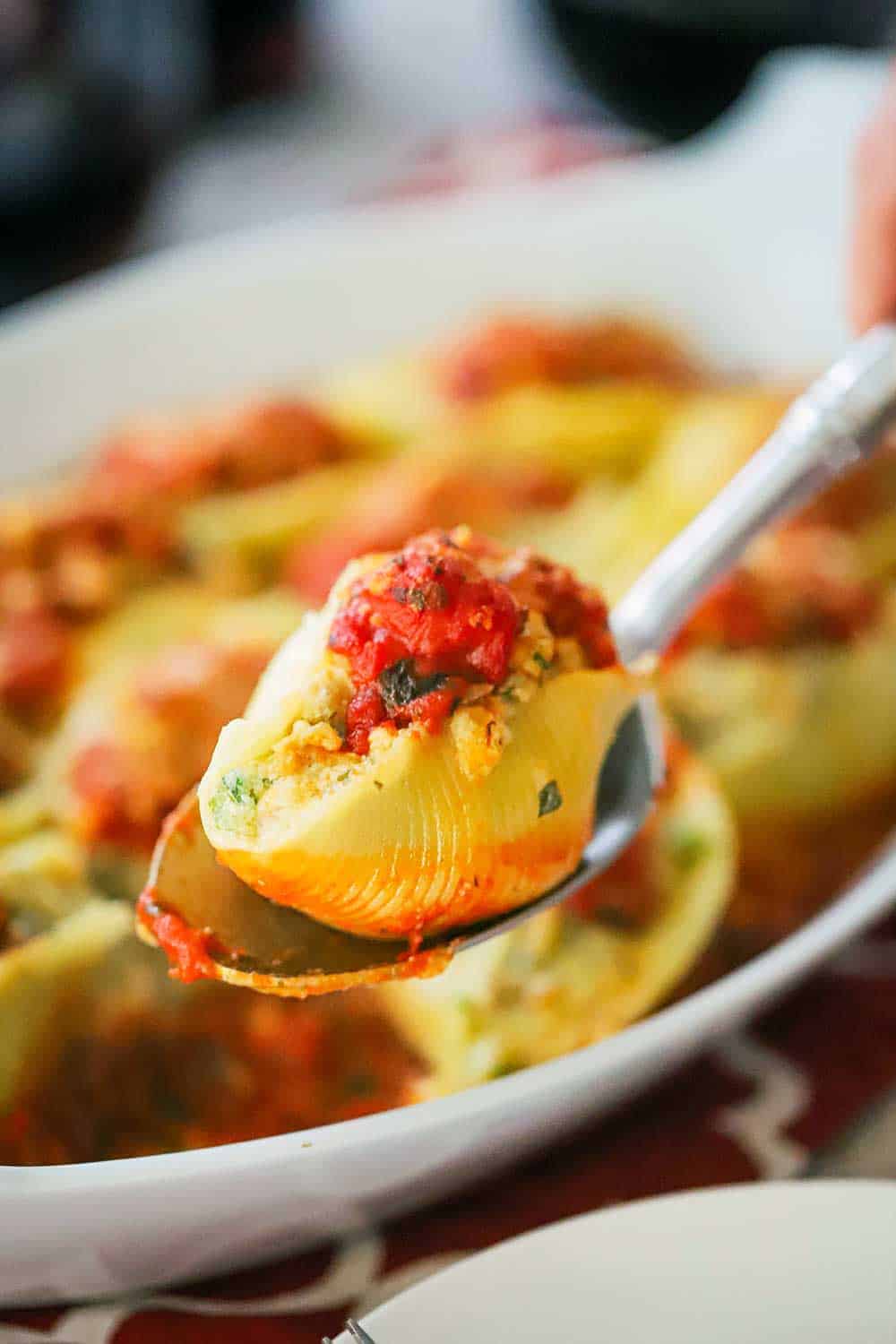 An Italian stuffed shell being held up on a large silver spoon. 