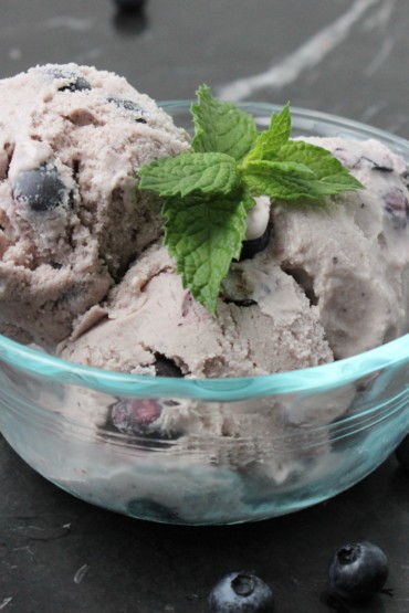 Homemade blueberry ice cream in a glass bowl with blueberries around it